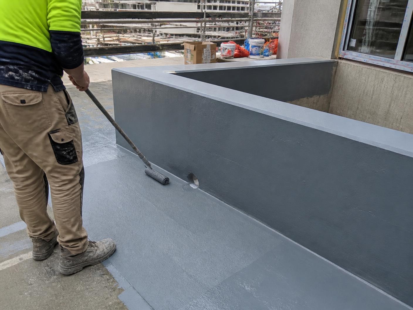 Waterproofing membrane being roller-applied to a concrete planter box and balcony substrate on a Sydney construction site